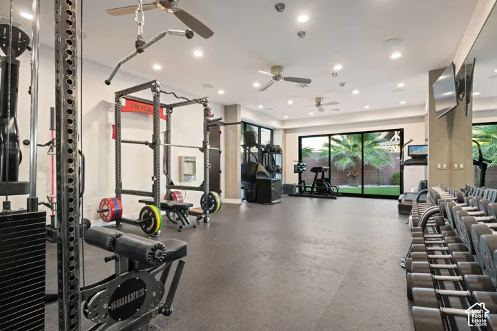 Spacious fitness room featuring rubberized flooring, recessed lighting, multi-blade ceiling fans, wall-to-wall mirror, and floor-to-ceiling sliding glass doors