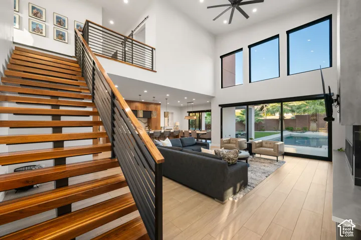 Open-concept interior featuring a floating staircase with wood treads and horizontal metal railings, expansive multi-story windows, wood-finish flooring, and a sliding glass door system
