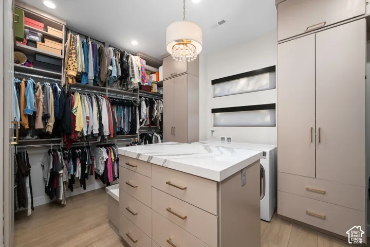 Custom cabinetry with metallic hardware, central island featuring a light-toned stone-surface countertop, wood-finish flooring, integrated shelving, and hanging pendant lighting