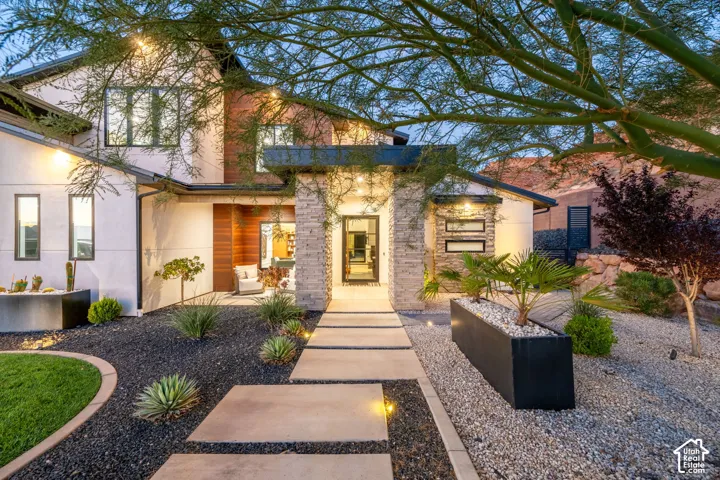 Modern architectural exterior featuring smooth stucco siding, natural stone veneer columns, wood-paneled accents, and a wide concrete paver walkway