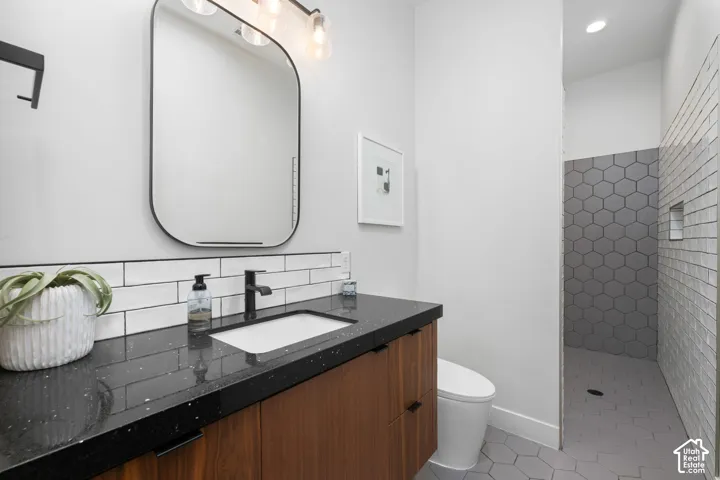 Bathroom featuring a wood-finish vanity, dark stone countertop with integrated sink, matte black faucet, subway-tile backsplash, and hexagon tile flooring
