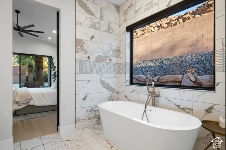 Freestanding soaking tub with a floor-mounted brushed metal faucet, large-format tile wall cladding, linear accent tiling, and a picture window