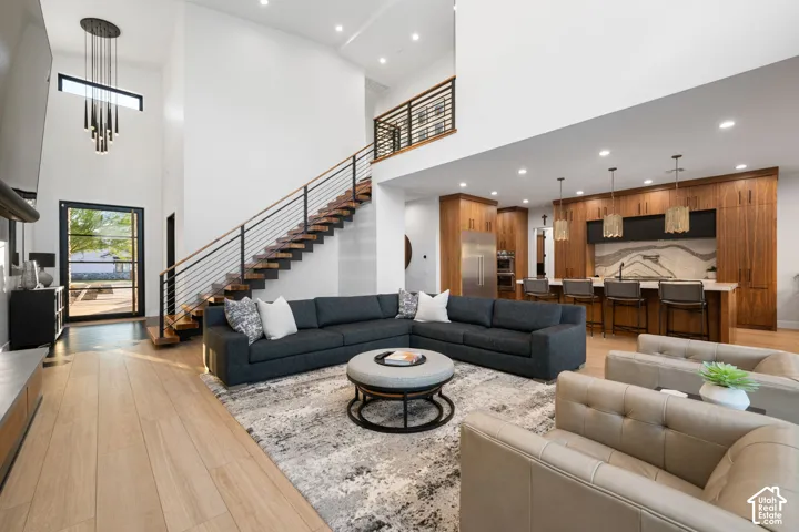Open-concept interior featuring double-height ceilings, a floating wood-tread staircase with horizontal metal railing, wood-finish flooring, custom wood cabinetry, and recessed lighting