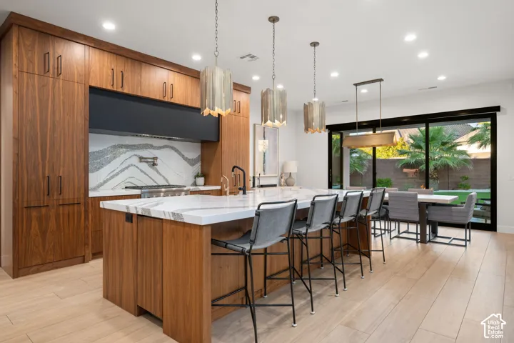 Kitchen featuring full-height wood-finish cabinetry, a waterfall-edge stone island with an integrated sink, a dramatic stone slab backsplash, and multi-paneled sliding glass doors