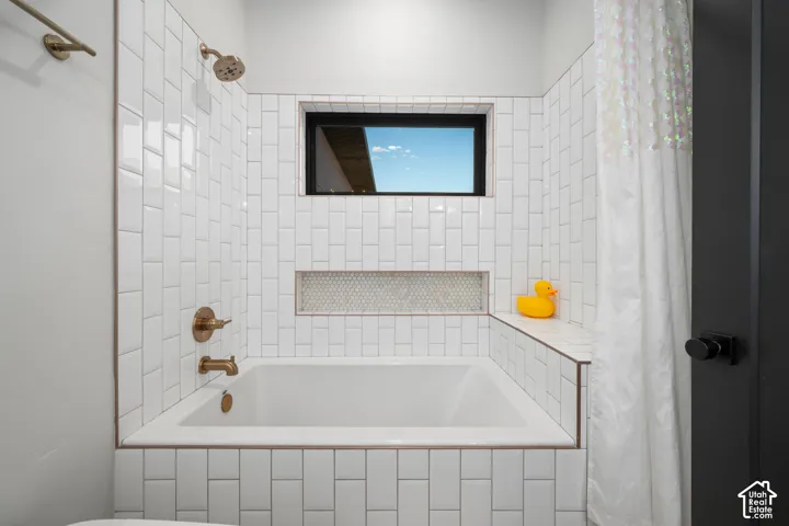 Built-in soaking tub with a tiled surround featuring vertical subway tiles, a recessed tile niche, brass-finish fixtures, and a horizontal window
