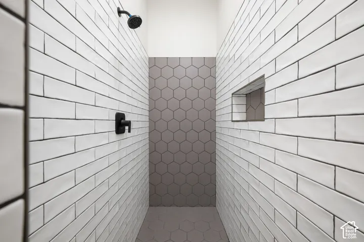 Walk-in shower featuring white subway wall tile, grey hexagonal tile flooring and accent wall, built-in recessed wall niche, and matte black plumbing fixtures