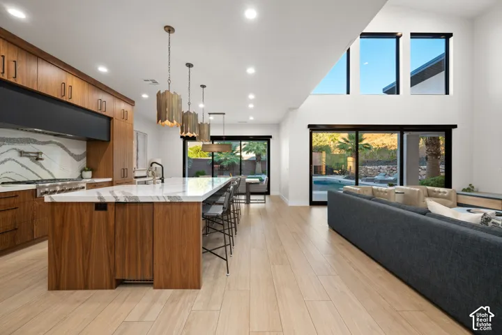 Kitchen featuring wood-finish cabinetry, stone-surface waterfall island, multi-level ceiling with recessed lighting, and expansive glass sliding doors