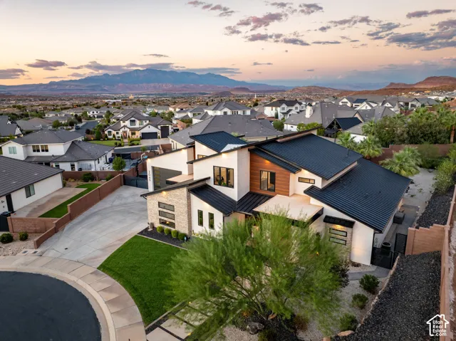 Modern architectural exterior featuring metal roofing, stacked stone accents, horizontal wood-finish siding, multi-level rooflines, and a concrete driveway