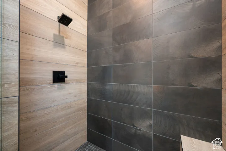 Shower enclosure featuring light and dark large-format tile walls, matte black rainfall showerhead, and matte black handle control