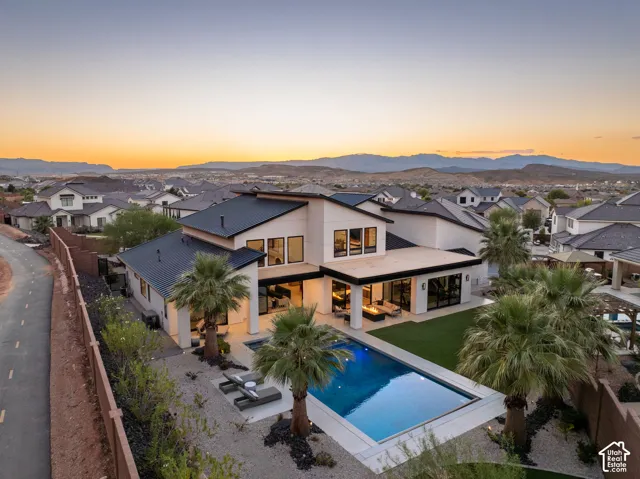 Contemporary multi-level residence featuring a metal roof, swimming pool, manicured lawn, covered patio with built-in fire feature, and mountain backdrop
