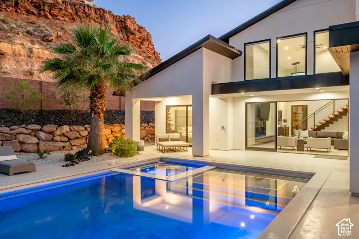 Contemporary exterior featuring a tiered natural stone retaining wall, recessed pool with integrated spa, large-format concrete patio, and floor-to-ceiling sliding glass doors