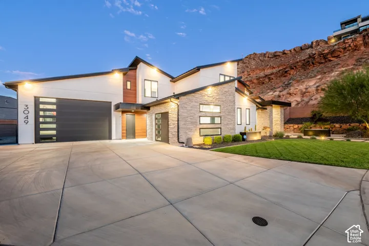 Modern exterior featuring stacked stone masonry, horizontal wood-finish siding, concrete driveway, multi-pane garage door with translucent glass inserts, and low-profile rooflines