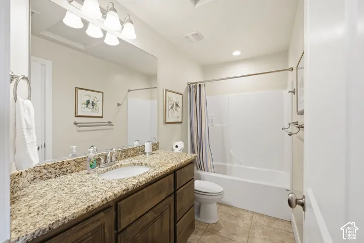 Bathroom featuring a stone-surfaced vanity with an integrated basin, dark wood-finish cabinetry, full-width vanity mirror, four-light fixture, and a tub-shower combination with tile flooring