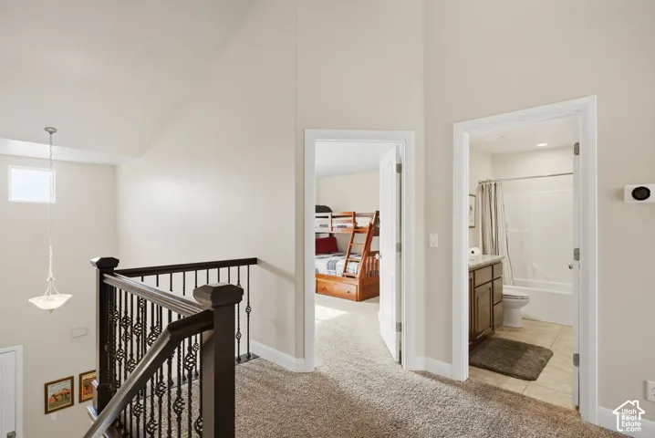 Vaulted ceiling, metal spindle railing, and neutral wall-to-wall carpeting