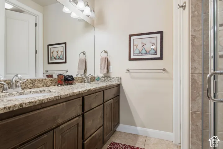 Bathroom featuring a dual-sink vanity with stone countertops, dark-finish cabinetry, a large wall-mounted mirror, and a glass-enclosed shower with tile surround