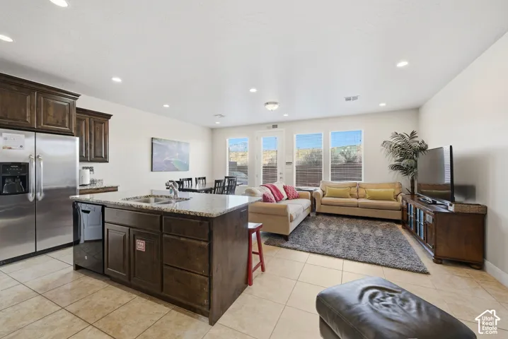 Kitchen featuring wood cabinetry, stone countertops, a center island with a double basin sink, tile flooring, and recessed lighting
