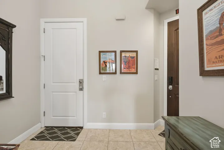 Entryway featuring large-format neutral floor tile, a solid-core white door with brushed metal hardware, and a stained wood-finish door with integrated electronic lock