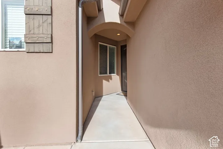 Stucco exterior entrance featuring an arched recessed portico, concrete walkway, and decorative wood-finish shutters