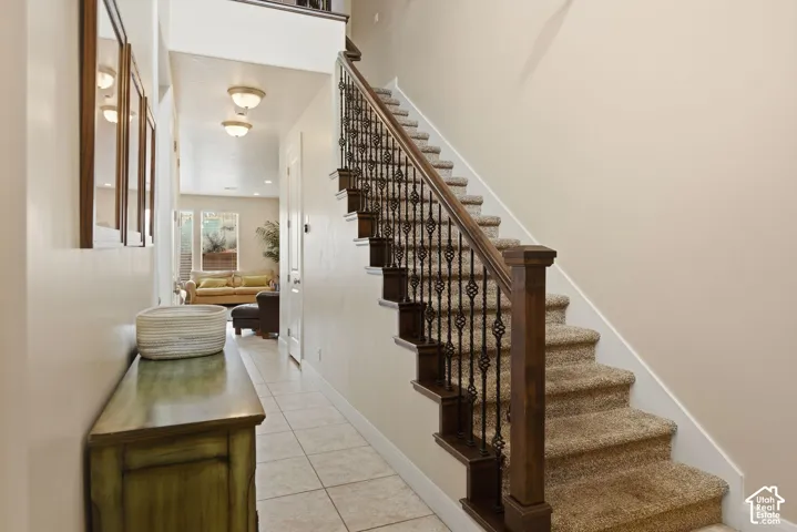 Staircase featuring a stained wood handrail, dark iron balusters, and carpeted treads, complemented by tile flooring and recessed lighting
