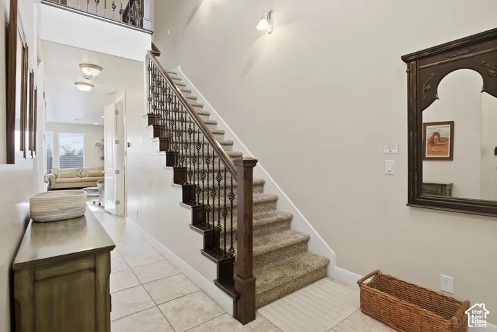 Entryway featuring a two-story ceiling, decorative metal balusters, dark wood-finish handrail, and ceramic tile flooring