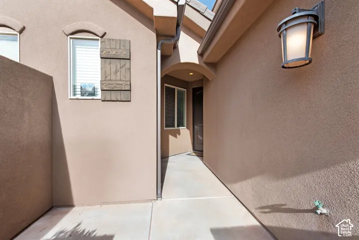 Stucco exterior entryway featuring a concrete walkway, decorative wooden shutters, an arched entry detail, and a wall-mounted lantern-style light fixture