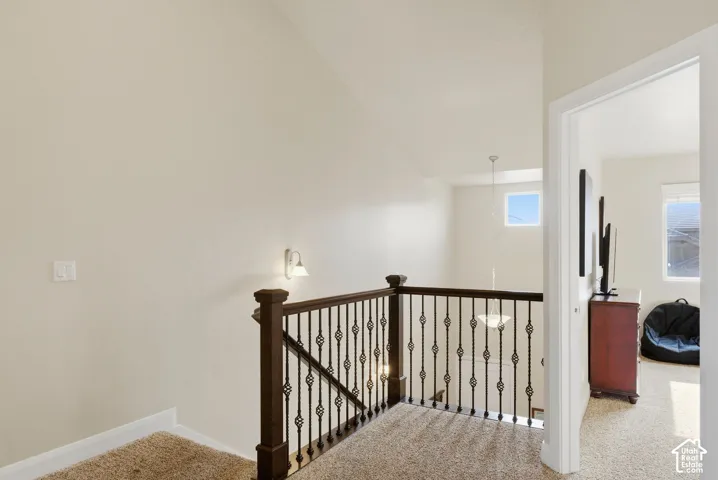 Vaulted ceilings, dark wood-finished handrail, decorative metal balusters, and wall-mounted lighting