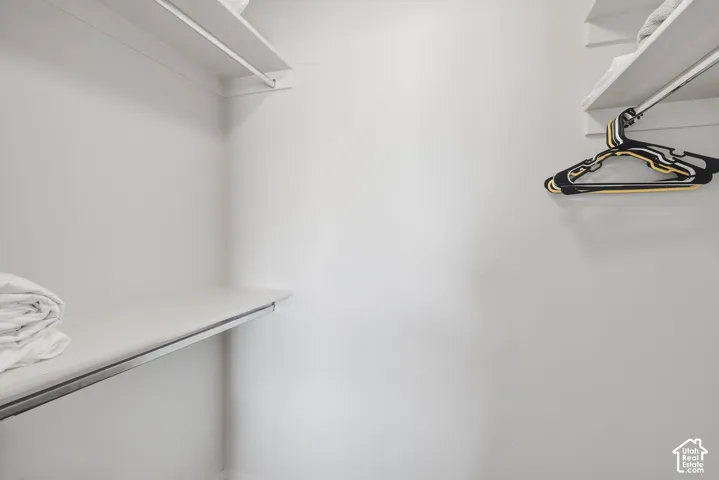 Storage closet featuring white built-in shelving and metal garment rods