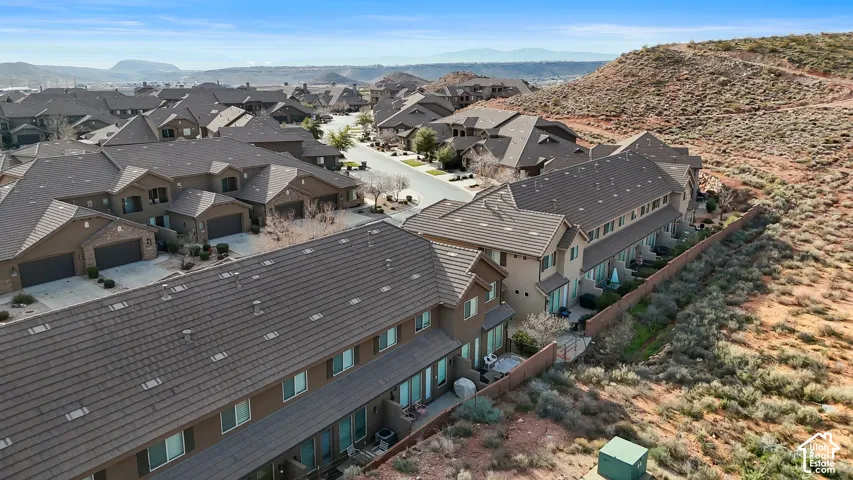 Aerial perspective of a multi-unit residential complex featuring multi-level construction, brown tile rooflines, stucco siding, and rear-facing patio spaces bordering a natural landscape