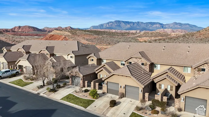 Multi-unit residential complex with stucco exterior, stone facade accents, concrete tile roofing, multi-car garages, and mountain backdrop