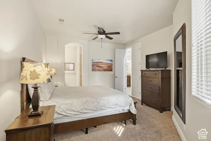 Neutral-toned room featuring high ceilings, an arched entryway, integrated ceiling fan with light fixture, carpeted flooring, and window blinds