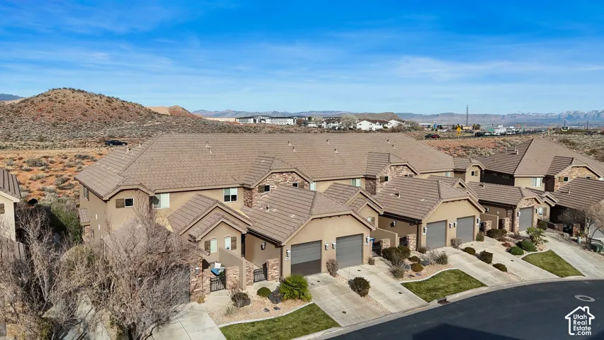 Multi-unit residential complex featuring stucco exterior walls, stone veneer accents, concrete tile roofing, and attached multi-car garages, set against a desert landscape