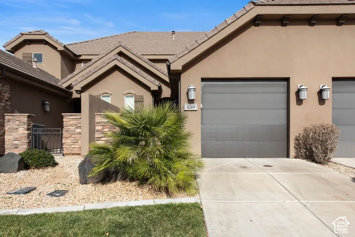 Stucco exterior featuring stacked stone masonry accents, multi-gabled roofline, concrete driveway, and wall-mounted exterior lighting