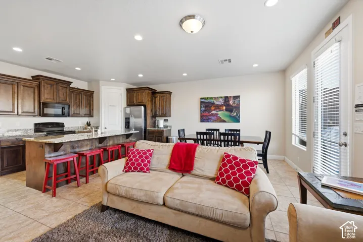 Kitchen featuring stained wood cabinetry, stone countertops, a central island with bar seating, tile flooring, and recessed lighting