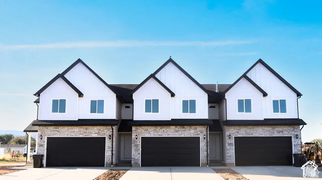 Multi-unit exterior featuring vertical board-and-batten siding, stacked stone masonry, three-car garage configuration, and multiple gabled rooflines