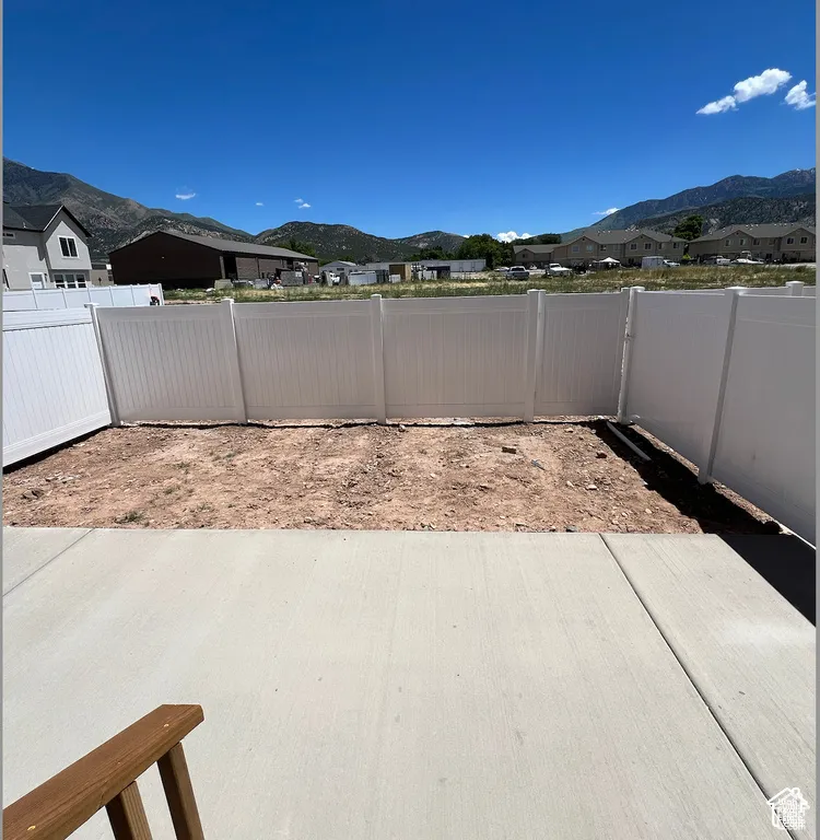 Rear exterior space featuring a concrete patio, white vinyl privacy fencing, and mountain scenery