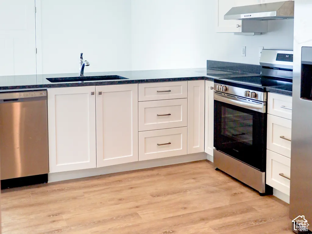Kitchen featuring white shaker-style cabinetry, dark stone countertops, stainless steel appliances, and wood-finish flooring
