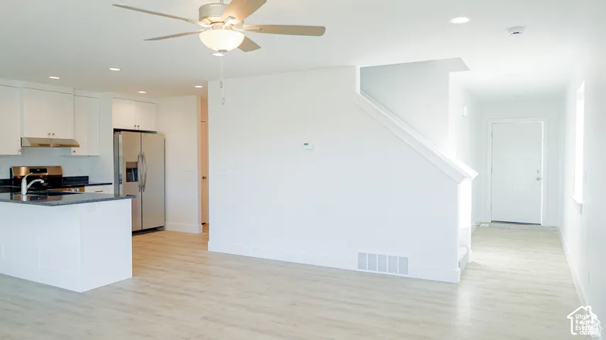 Open-concept interior featuring white shaker cabinetry, stainless steel appliances, dark stone countertops, wood-finish flooring, and a ceiling fan with integrated lighting