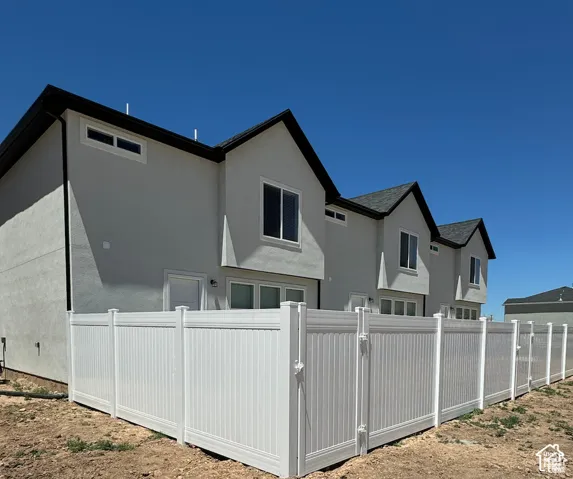 Multi-unit exterior featuring light-toned stucco siding, dark roof gables, and a full-height white vinyl privacy fence