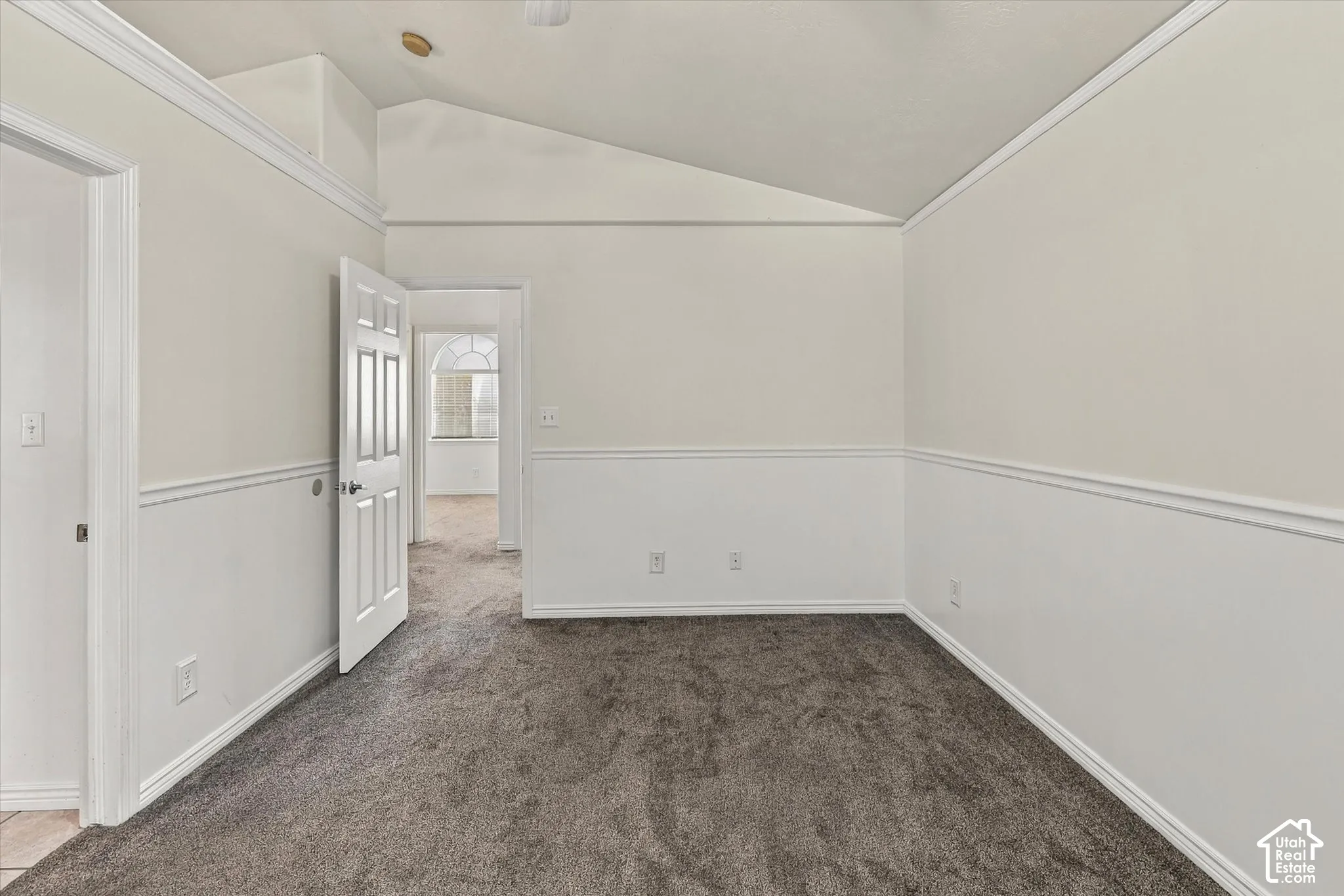 Vaulted ceiling, chair rail molding, six-panel interior door, and neutral wall-to-wall carpeting