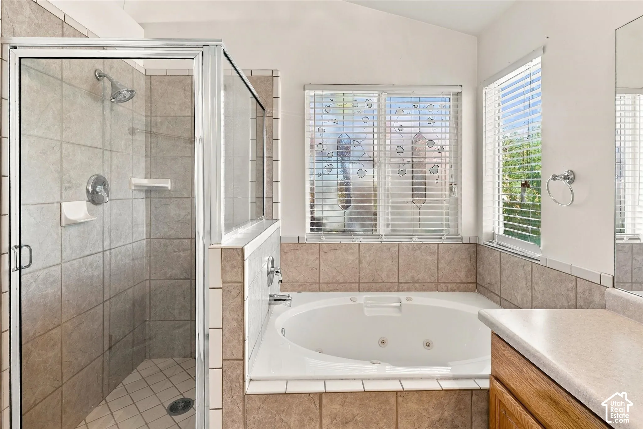 Walk-in glass-enclosed shower featuring tile surround, oversized soaking tub with tile deck, and neutral tile wall accents