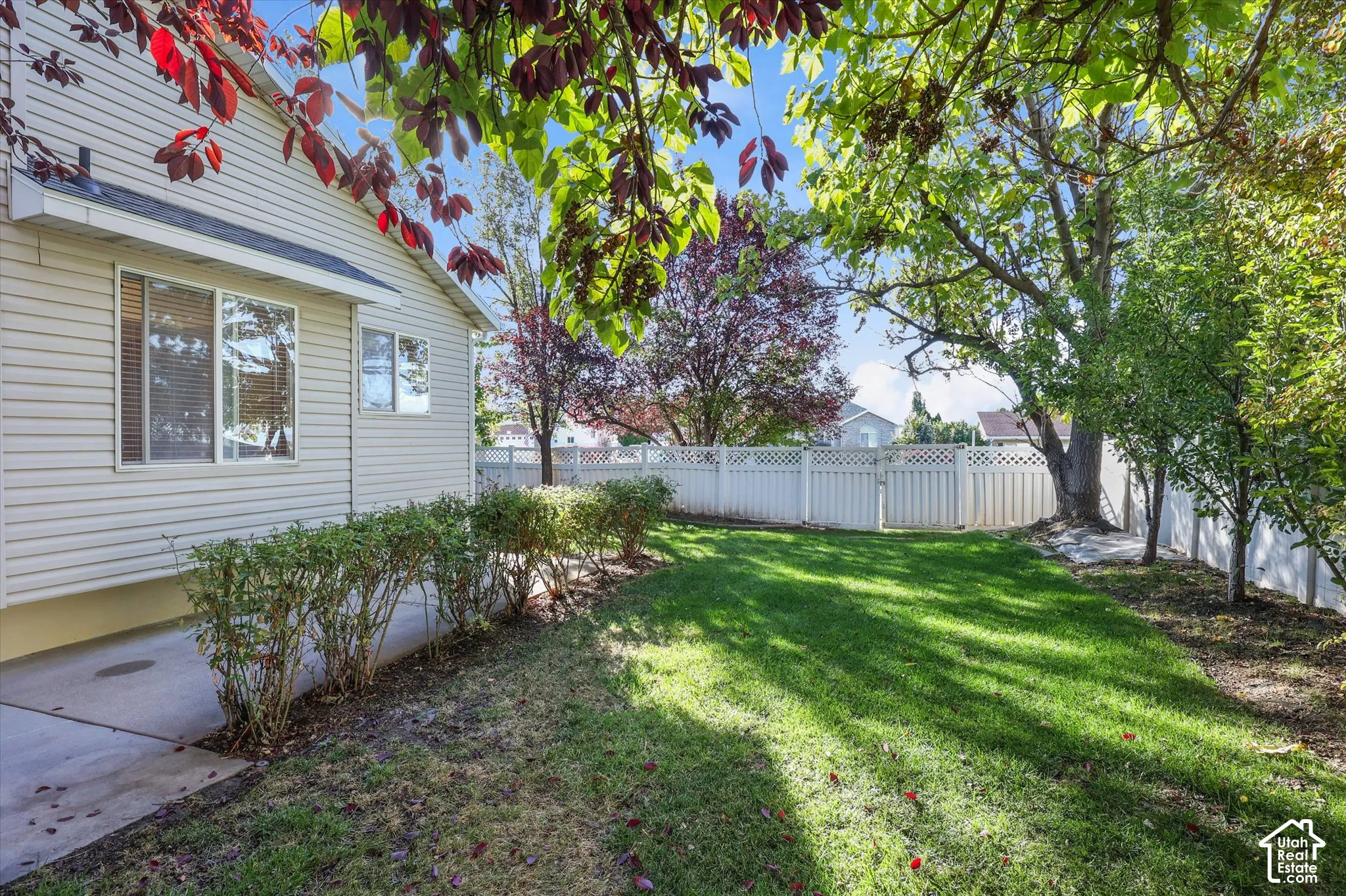 Backyard featuring a concrete patio, perimeter vinyl fencing, a grass lawn, and mature trees