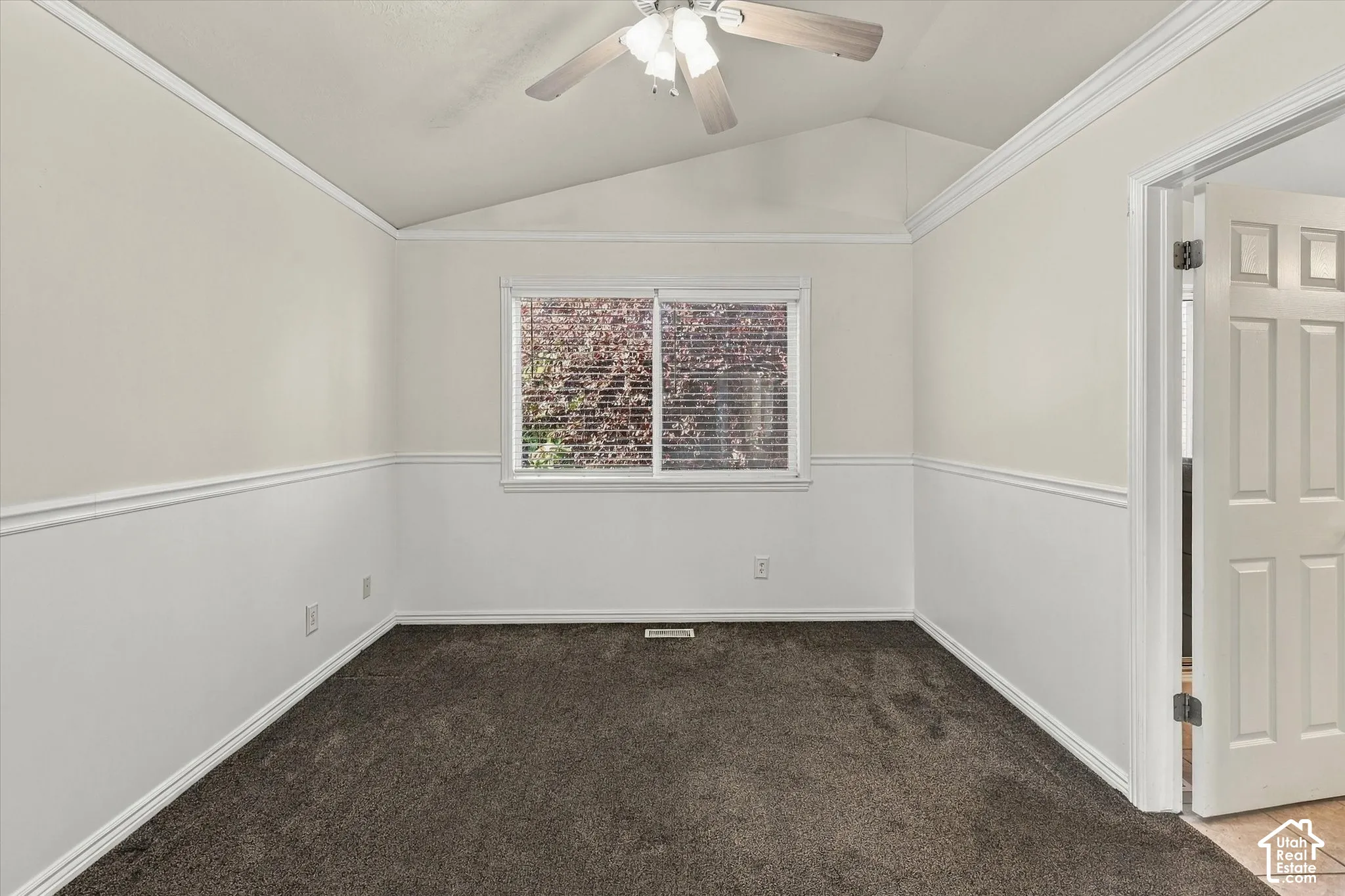 Vaulted ceiling featuring a central light fixture and ceiling fan, chair rail molding, and carpeting