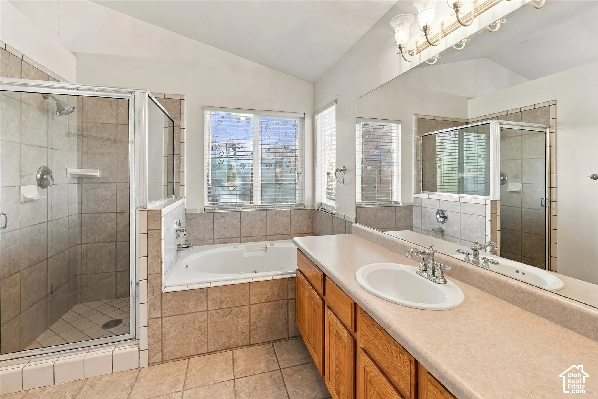 Bathroom featuring a built-in soaking tub, separate tiled shower with glass enclosure, wood cabinetry, large vanity mirror, and dual-basin countertop