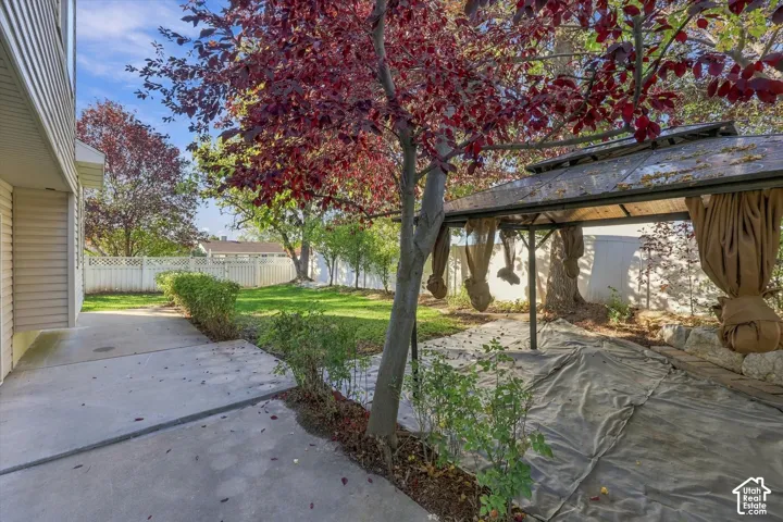 Backyard featuring a concrete patio, mature trees, and white vinyl privacy fencing