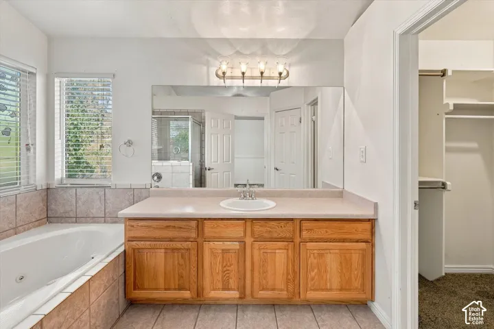 Bathroom featuring a wood-finish vanity with a drop-in sink, a built-in jetted soaking tub with tile surround, a large wall-mounted mirror, and a walk-in closet with built-in shelving