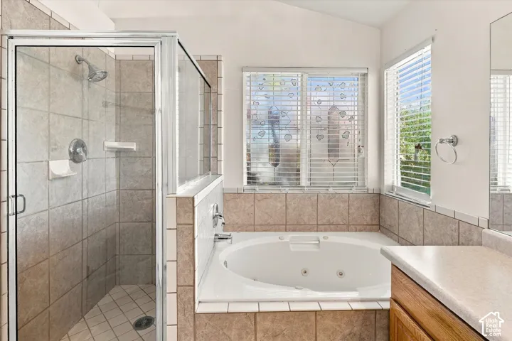 Walk-in glass-enclosed shower featuring tile surround, oversized soaking tub with tile deck, and neutral tile wall accents