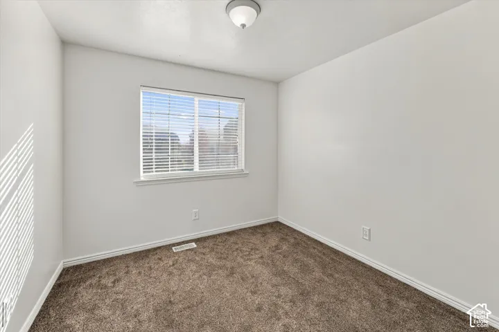Neutral-toned interior space featuring neutral wall-to-wall carpeting, a single window with horizontal blinds, and a central ceiling-mounted light fixture