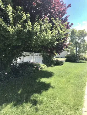 Expansive lawn area featuring mature trees, landscaped shrubbery, and white vinyl lattice-top fencing