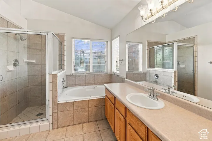Bathroom featuring a built-in soaking tub, separate tiled shower with glass enclosure, wood cabinetry, large vanity mirror, and dual-basin countertop