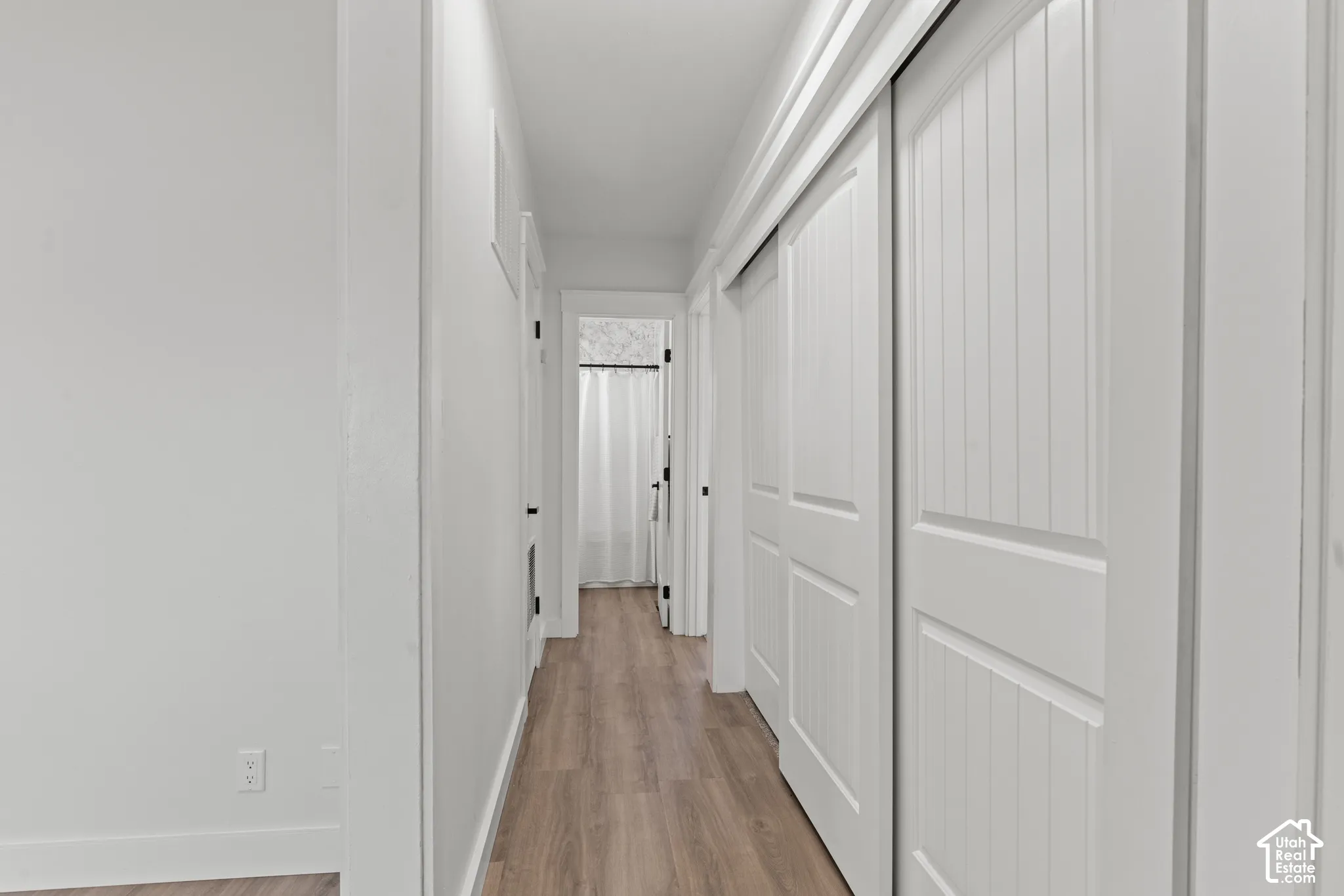 Hallway featuring wood-finish flooring, white panel-style doors, and sliding closet doors with vertical detailing